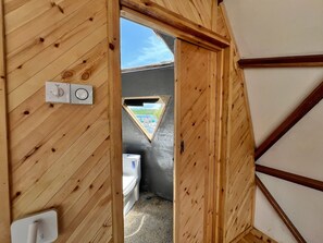 Ein Badezimmer mit Holzvertäfelung, einer Toilette, einem Timer und einem kleinen Fenster.