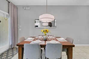 A dining room with a wooden table set for four, a vase of yellow flowers, and a modern pendant light. - Welcoming Townhome 4BD3BA at Paradise Palms PP8955 (Kissimmee)