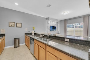 A modern kitchen with granite countertops, wooden cabinets, a stainless steel sink, and a trash can. - Welcoming Townhome 4BD3BA at Paradise Palms PP8955 (Kissimmee)