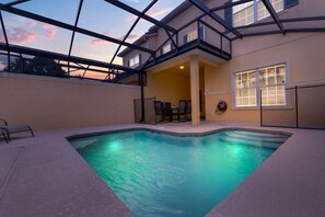 A swimming pool with a glass ceiling, a covered patio with chairs, and a view of the sunset. - Welcoming Townhome 4BD3BA at Paradise Palms PP8955 (Kissimmee)