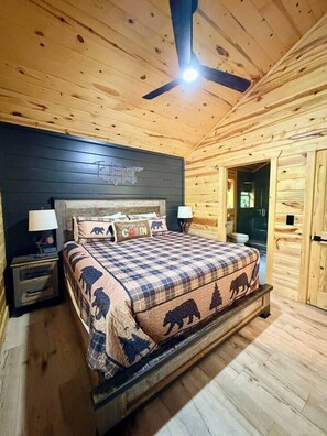 Una camera da letto in stile baita con un letto, comodini, una ventola a soffitto e una porta che dà su un'altra stanza.