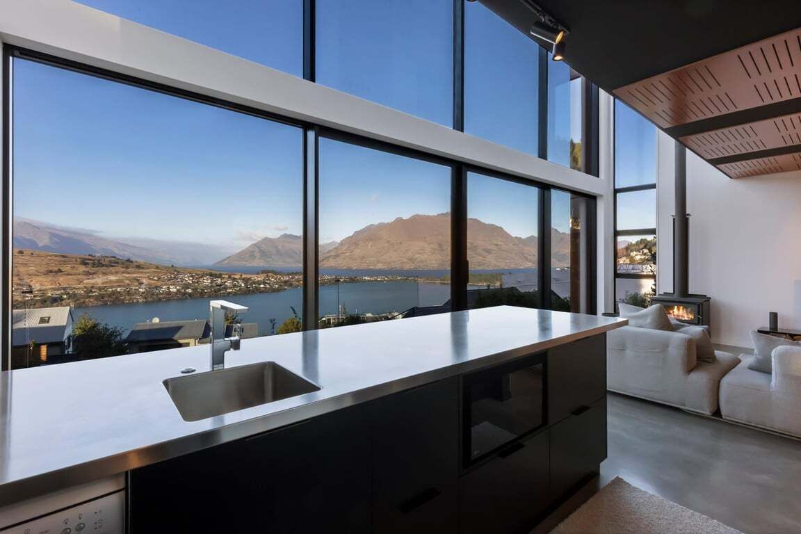 Una cocina moderna con un ventanal grande, estufa integrada y vistas a un lago y montañas.
