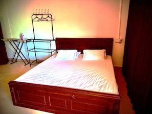 A neatly made bed with a wooden headboard, a small table with an ironing board, and a wall-mounted drying rack.