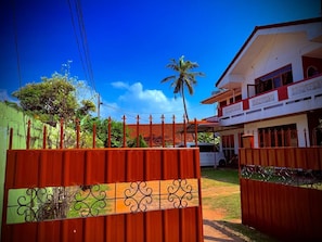 A gated property with a red fence, a white building with balconies, and a palm tree in the background.