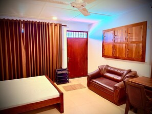 Um quarto com cama, sofá de couro, escrivaninha de madeira, ventoinha no teto e guarda-roupa.