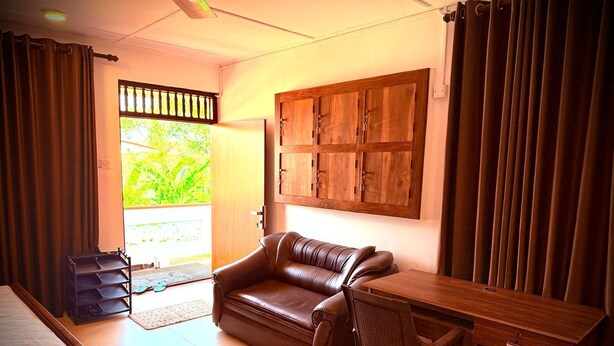 A room with a bed, a leather sofa, a wooden desk, and a view of greenery outside.