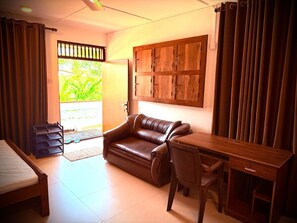 Quarto com cama, sofá de couro, escrivaninha de madeira e vista para o verde lá fora.
