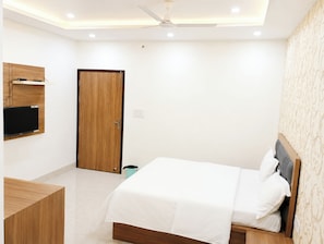 A bedroom with a bed, a TV mounted on the wall, a ceiling fan, and a wooden door. - Hotel Taha Inn Home Comfort (Srinagar)