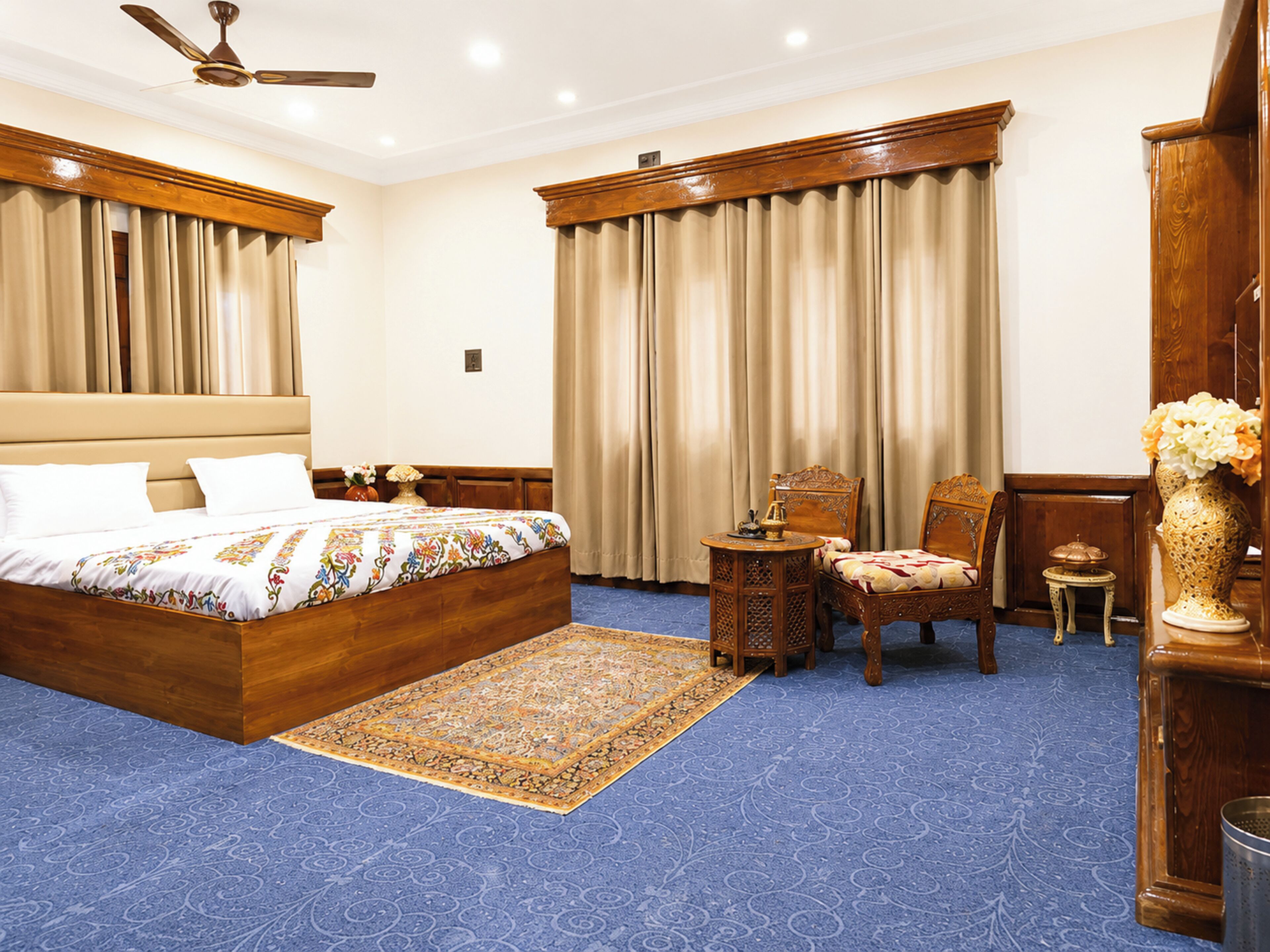 A spacious bedroom with a large bed, a sitting area with a chair and table, and a decorative vase.