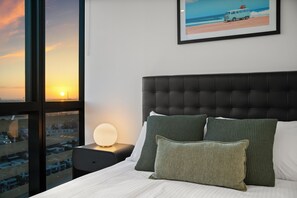 A hotel room with a large window, a bed with green and white bedding, a black headboard, and a framed picture of a beach scene. - Sub Penthouse in Docklands with Breathtaking 180° Views | Pool, Gym & Parking (Docklands)