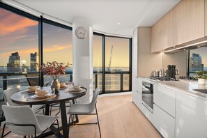 A modern kitchen with a large window, a dining area with a table set for two, and a view of the city skyline. - Sub Penthouse in Docklands with Breathtaking 180° Views | Pool, Gym & Parking (Docklands)