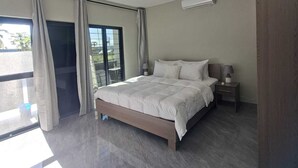 Une chambre moderne avec un grand lit, une table de chevet, un appareil de climatisation et une porte-fenêtre coulissante donnant sur un espace extérieur.