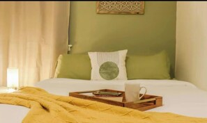A bed with a yellow blanket, a tray with a mug and a book, and a green wall with a geometric decoration.