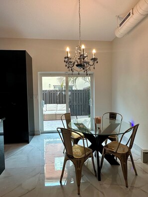 A dining area with a glass table and chairs, a chandelier, and a sliding glass door leading to a patio. - Spacious & Peaceful Downtown Living in St Pete (St. Petersburg)