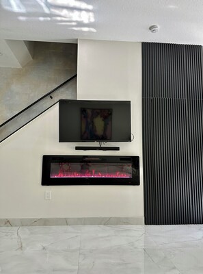 A modern living room with a flat-screen TV mounted on the wall, a built-in fireplace, and a staircase leading to an upper level. - Spacious & Peaceful Downtown Living in St Pete (St. Petersburg)