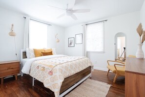 Een slaapkamer met een bed, een bureau, een stoel, een plafondventilator en een raam.