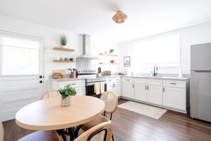 Een moderne keuken met witte kasten, een ronde houten tafel en een eetkamerstoel.