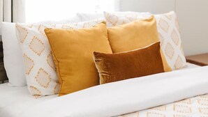 Una cama con almohadas estampadas, una lámpara colgante y un ventanal con cortinas.