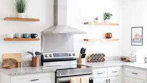 Una cocina moderna con extractor de acero inoxidable, repisas de madera con tazas, un juego de cuchillos y una botellera.