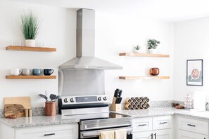 Una cocina moderna con extractor de acero inoxidable, repisas de madera con tazas, un juego de cuchillos y una botellera.
