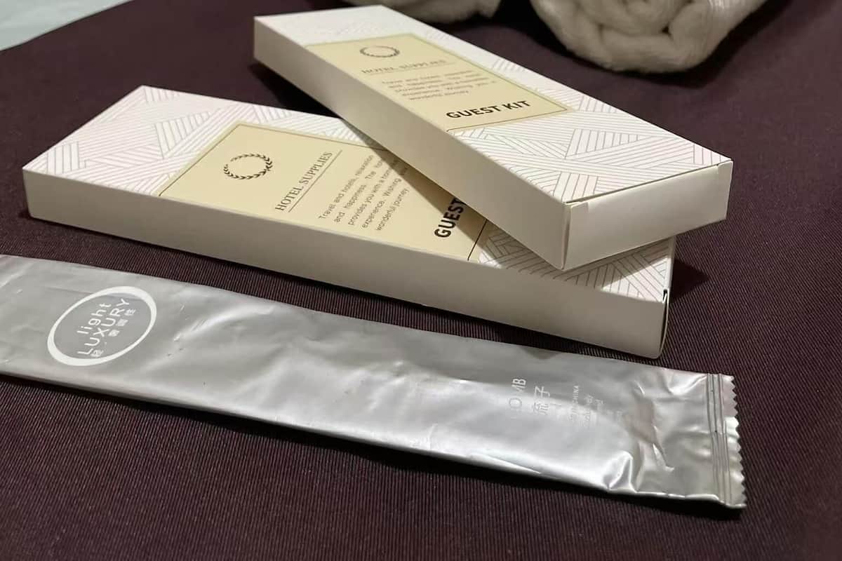 Una cama bien hecha con toallas blancas enrolladas, una caja de artículos de cortesía y un producto de cuidado de la piel sobre una superficie de tela oscura.
