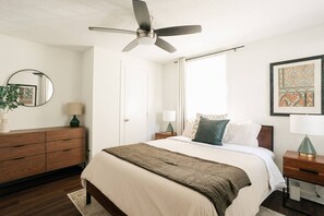 Ein Schlafzimmer mit einem Bett, einem Deckenventilator, einer Kommode und einem gerahmten Bild an der Wand.