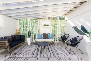 Eine überdachte Terrasse mit einem gemusterten Boden, einer Couch, zwei Stühlen und hängenden Pflanzen.
