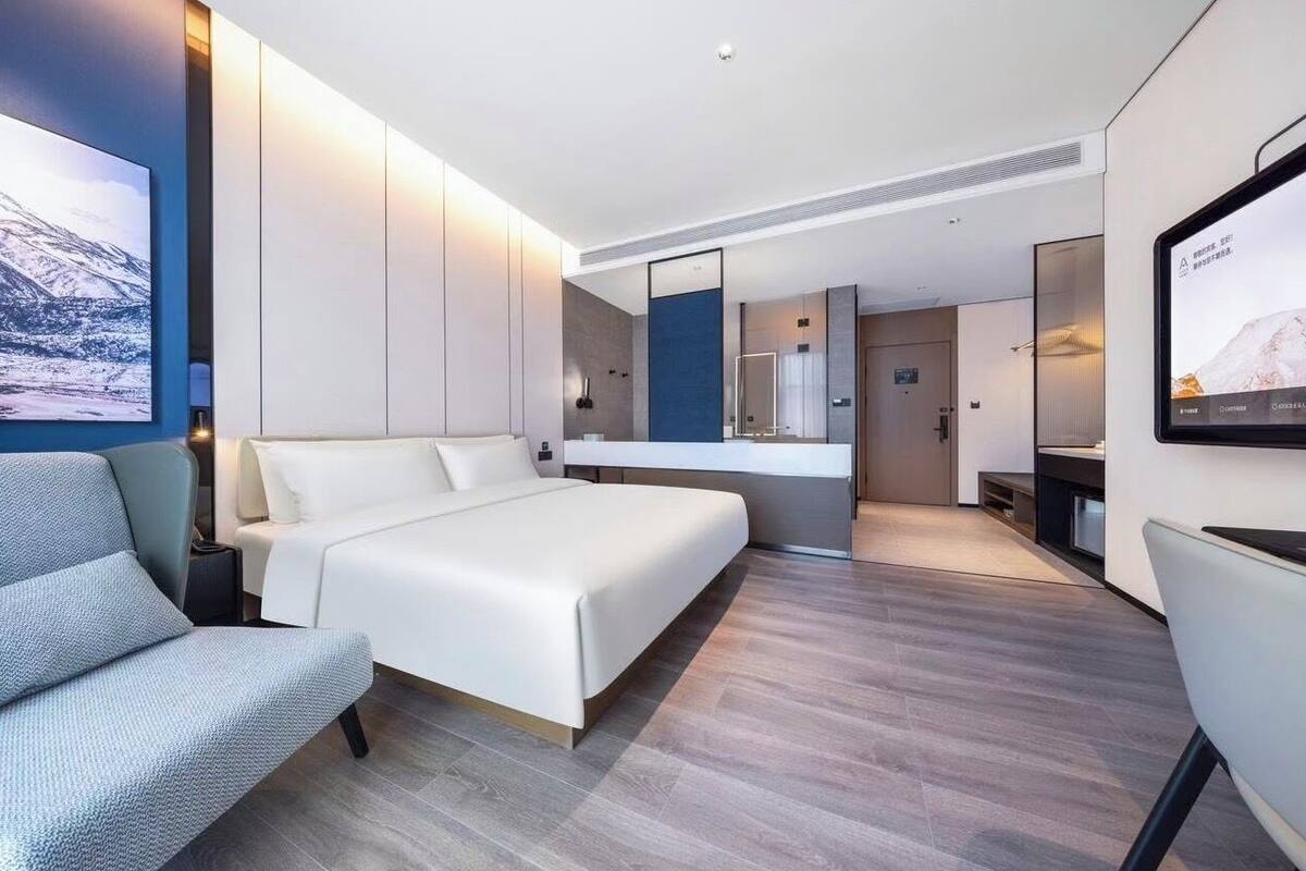 A modern hotel room with a large bed, a seating area, a bathroom, and a TV screen.
