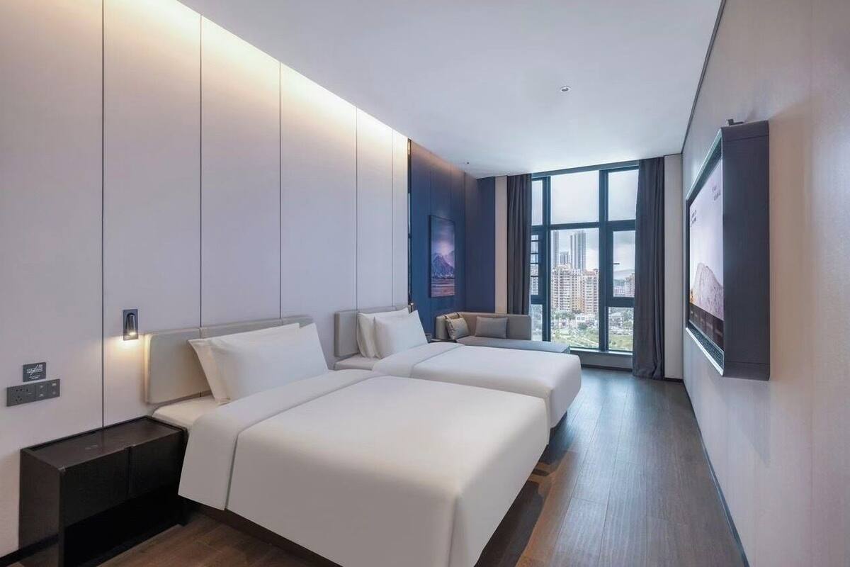 A modern hotel room with two beds, a large window, and a city view.