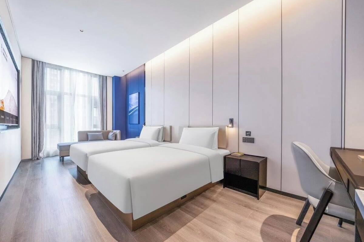 A modern hotel room with two beds, a desk, and a chair.