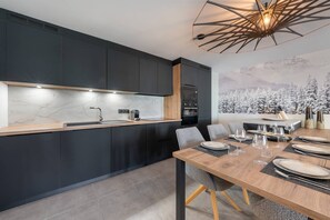 A modern kitchen with dark cabinetry, a marble countertop, and a dining area with a wooden table set for six. - Art Mony 209 (CHATEL)