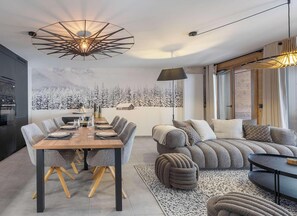 A modern living room with a sofa, a dining table set for six, and a kitchen area. - Art Mony 209 (CHATEL)
