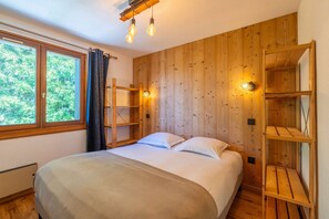 Ein Schlafzimmer mit Bett, Holzwandverkleidung, einem Fenster mit Vorhängen und eingebauten Regalen.