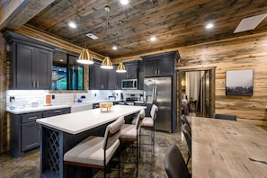 A modern kitchen with dark cabinetry, stainless steel appliances, and a large island with bar stools. - New Cabin/Hot Tub/Fire Pit/Arcade/Shuffleboard (Broken Bow)