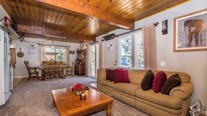 Una sala de estar acogedora con techo de madera, un sofá con cojines, una mesa de centro y una zona de comedor con sillas y una mesa.