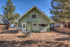 A single-story house with a green exterior, a front porch with a table and chairs, and a small attached garage. - Mountain Dream Lodge (Big Bear)