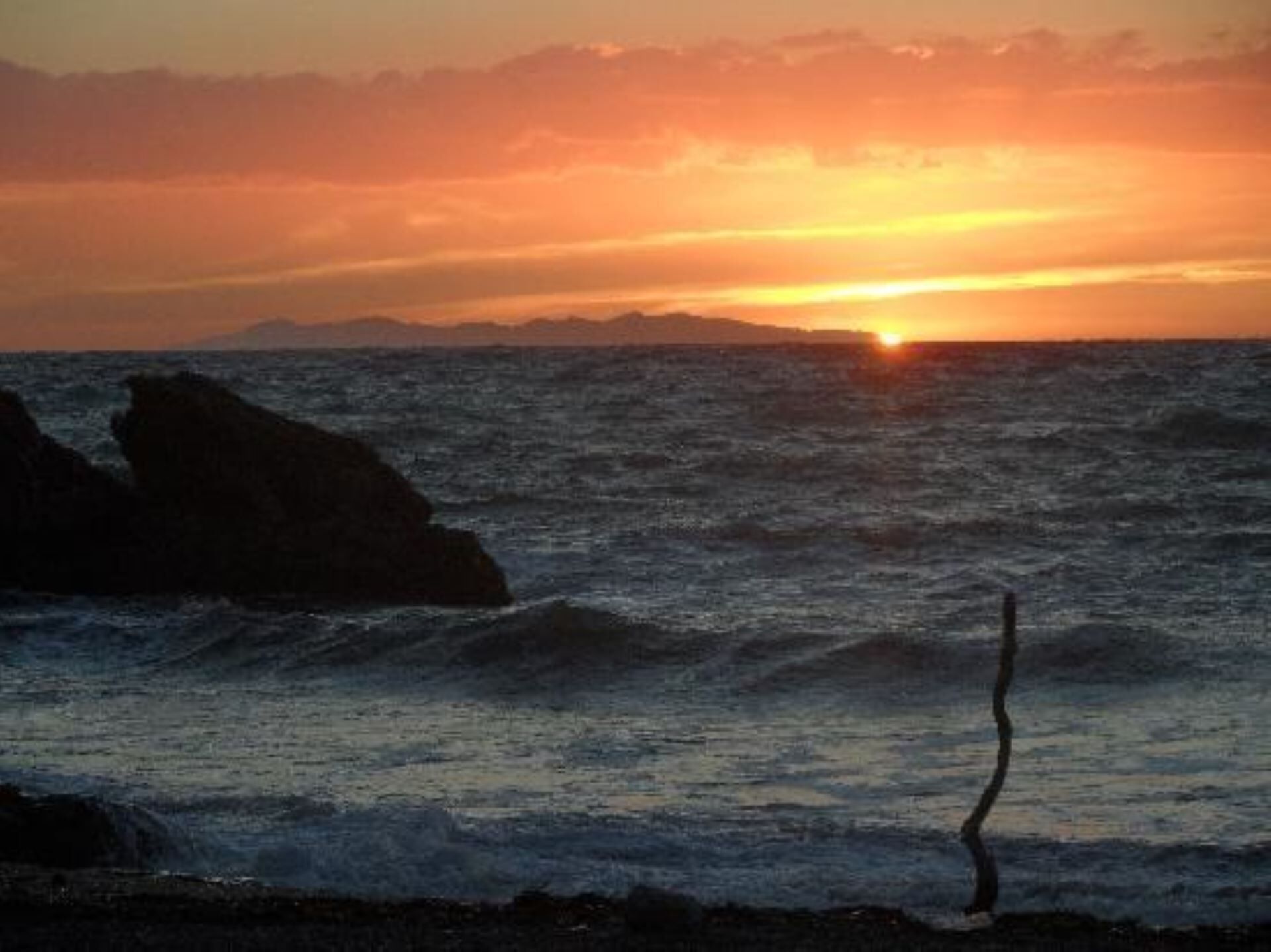 A sunset over the ocean with waves and rocks.