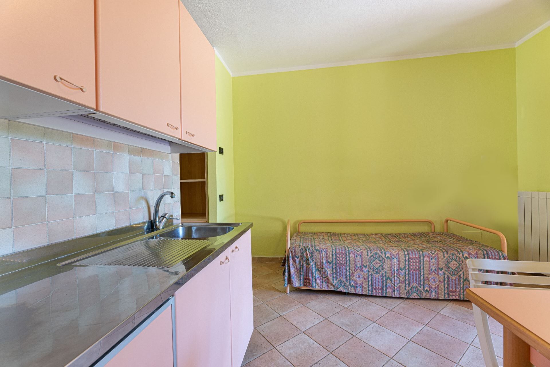 A compact kitchen with a sink, cabinets, and a bed with a patterned bedspread.