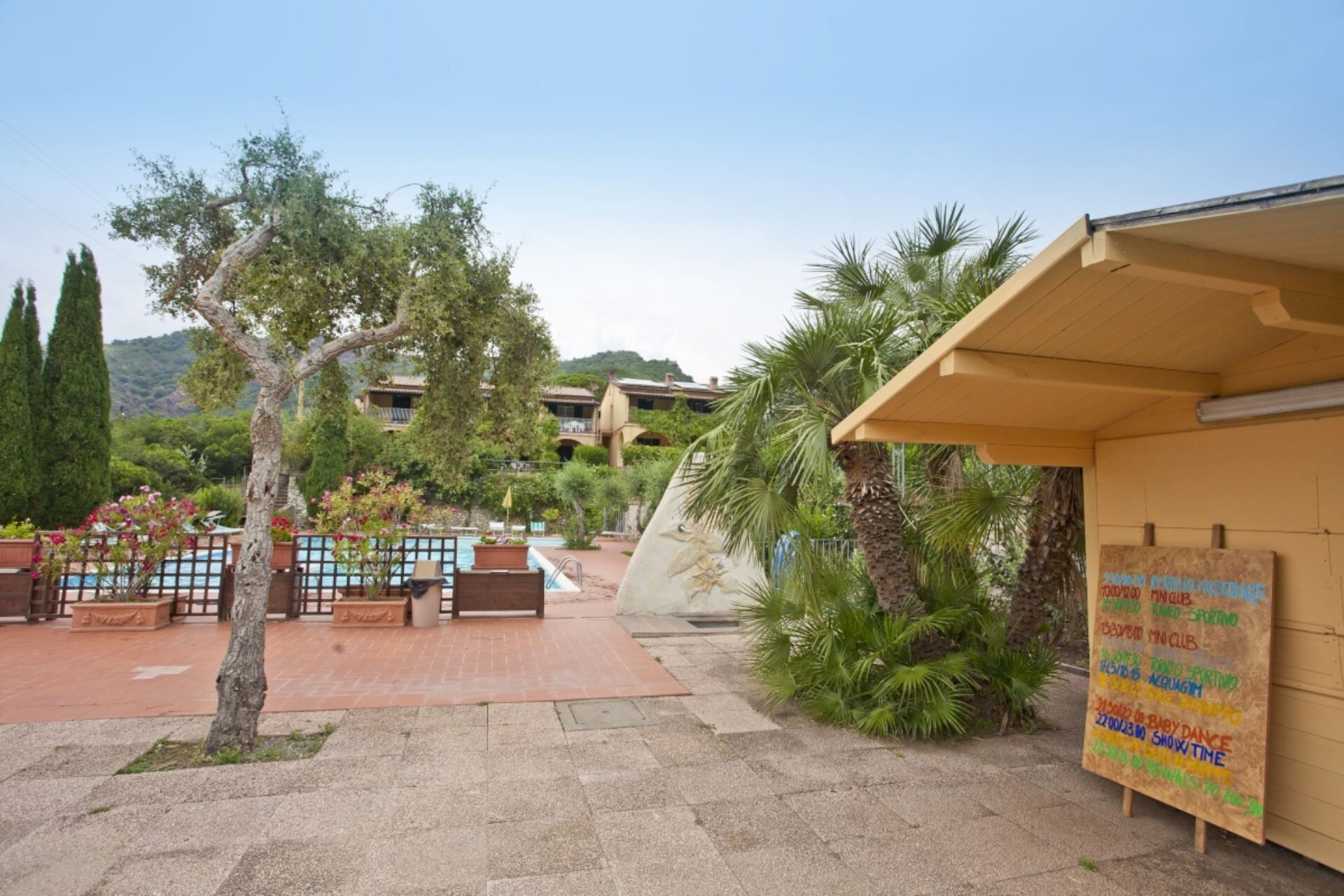 A courtyard with a pool, outdoor seating, and a signboard listing event times.