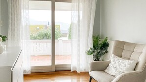 A room with a sliding glass door leading to a balcony, a beige armchair, a white rug, and a potted plant. - 3 bedroom cozy home in ålesund (Ålesund)