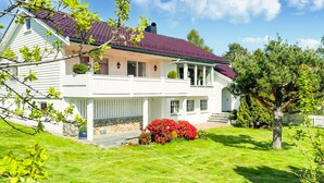 A two-story house with a red-tiled roof, a stone foundation, and a well-maintained lawn. - 3 bedroom cozy home in ålesund (Ålesund)