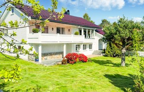Ein zweistöckiges Haus mit rotem Ziegeldach, steinernen Fundament und einem gepflegten Rasen.