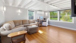 Una sala de estar moderna con un sofá seccional, una mesa de centro de madera, un escritorio con una computadora y un televisor montado en la pared.