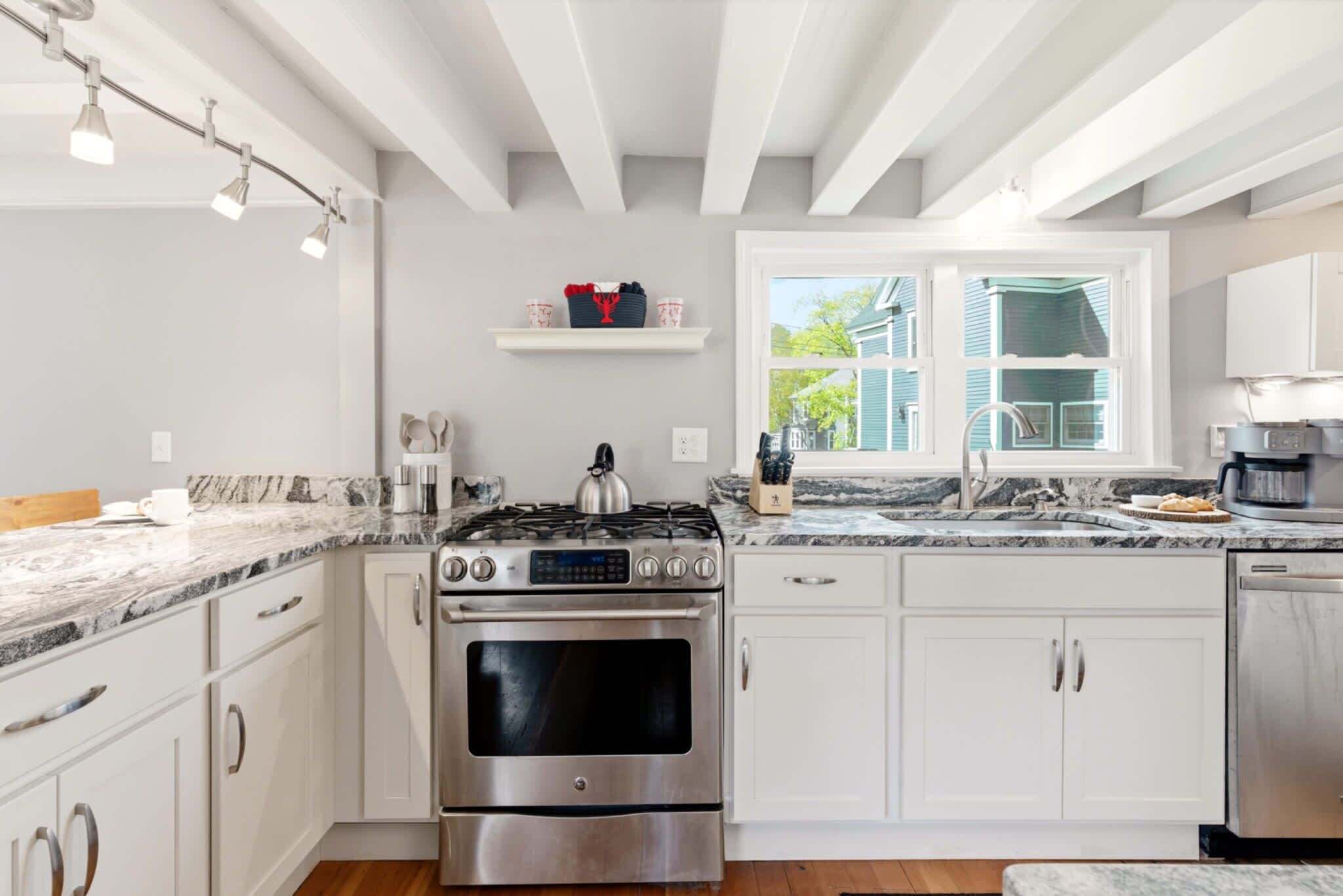 Une cuisine moderne avec des meubles blancs, une cuisinière en acier inoxydable et une fenêtre donnant sur une maison.
