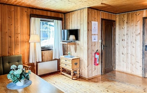 A wooden-paneled room with a television, a small cabinet, a radiator, a fire extinguisher, and a window with curtains. - Stunning home in Vinstra with sauna (Vinstra)