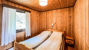 Una habitación de madera con una cama, una mesita de noche, una lámpara y una ventana con cortinas.