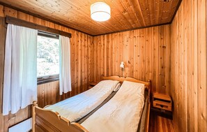A wooden room with a bed, a nightstand, a lamp, and a window with curtains. - Beautiful home in Vinstra with sauna (Vinstra)