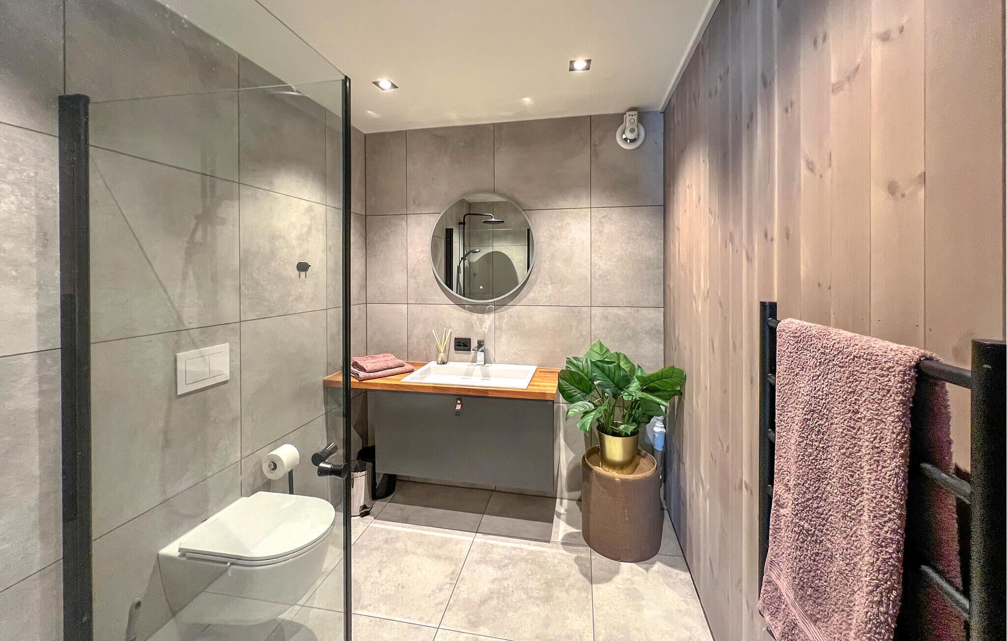 A modern bathroom with a glass-enclosed shower, a toilet, a sink with a mirror, and a towel rack.