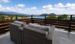 A balcony with wicker furniture and a view of a lake and mountains.