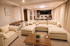 A modern living room with a sectional sofa, a wooden coffee table, and a dining area in the background.